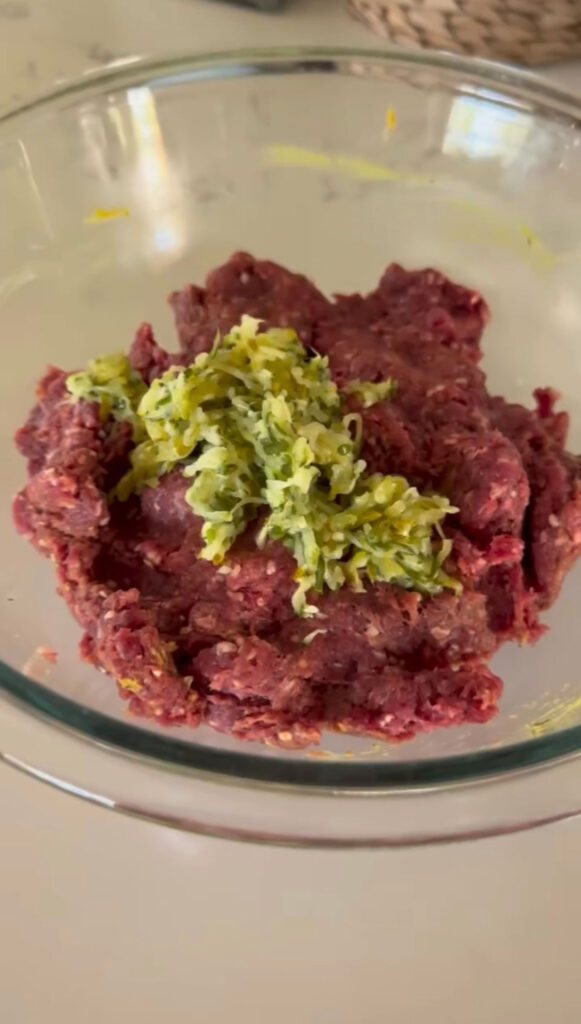 A glass bowl with ground beef mixture and grated pickles on top.