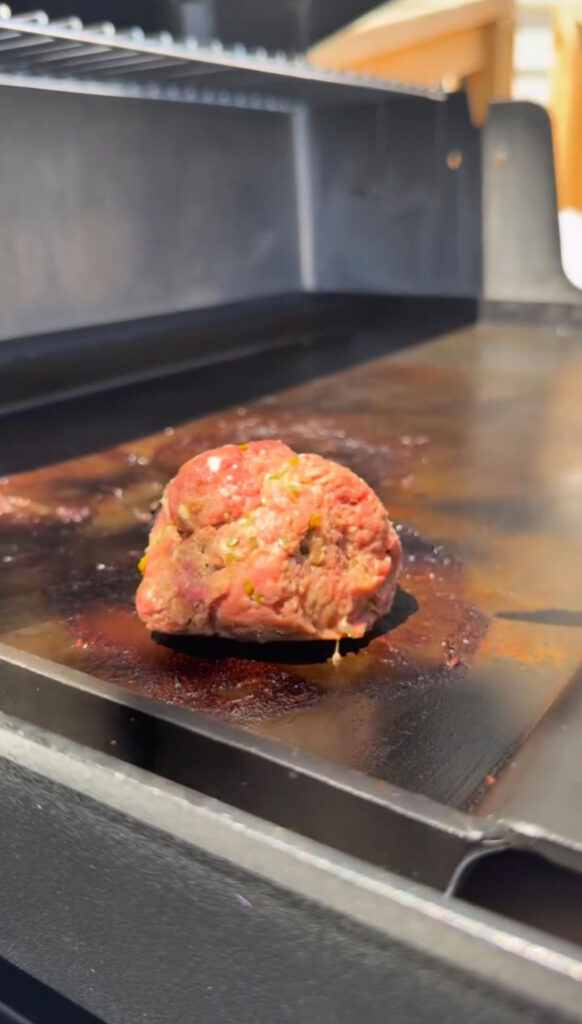 Ground beef pickle burger patty on a flat top.