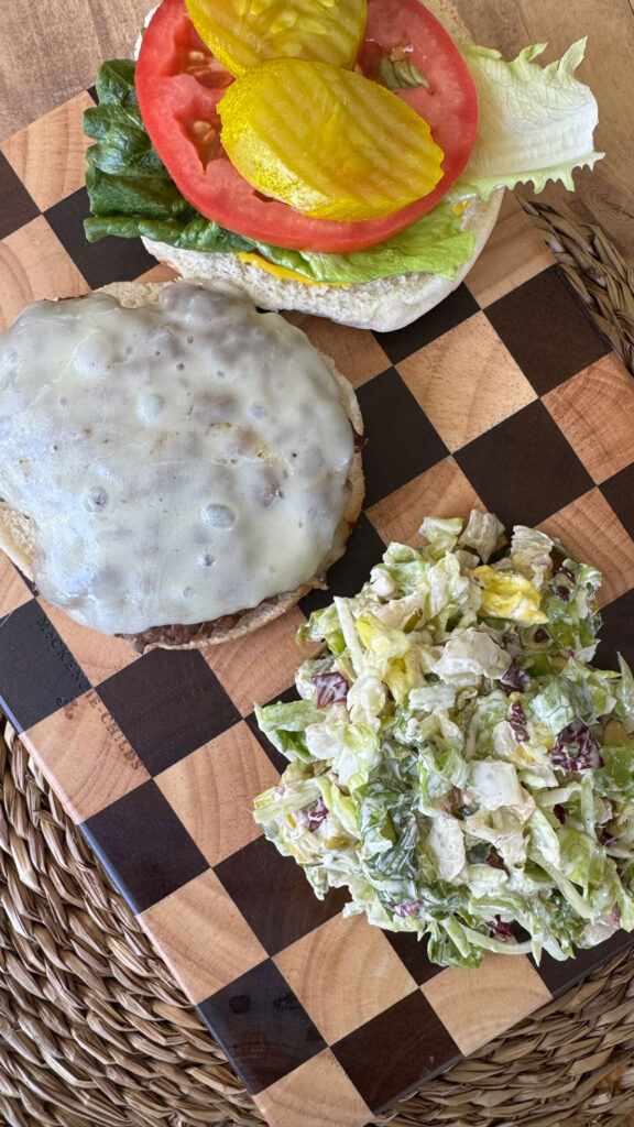Overhead image of a pickle burger on a checkered cutting board.