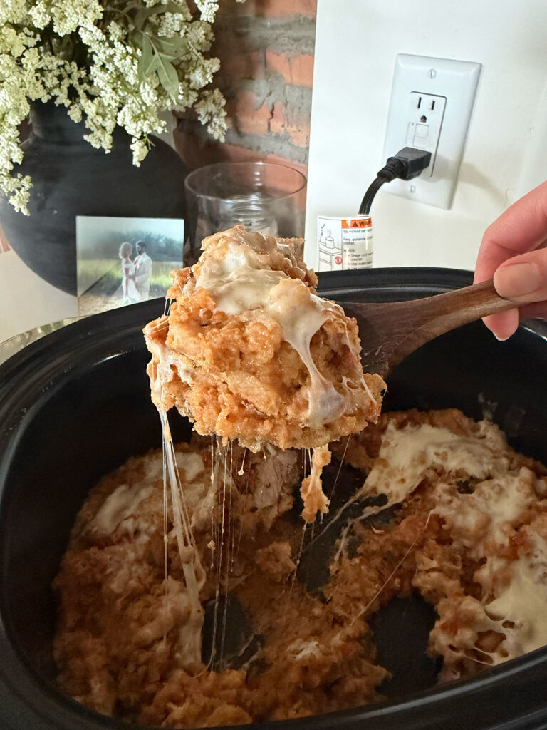 A hand scooping up bruschetta chicken with a wooden spoon from the slow cooker.