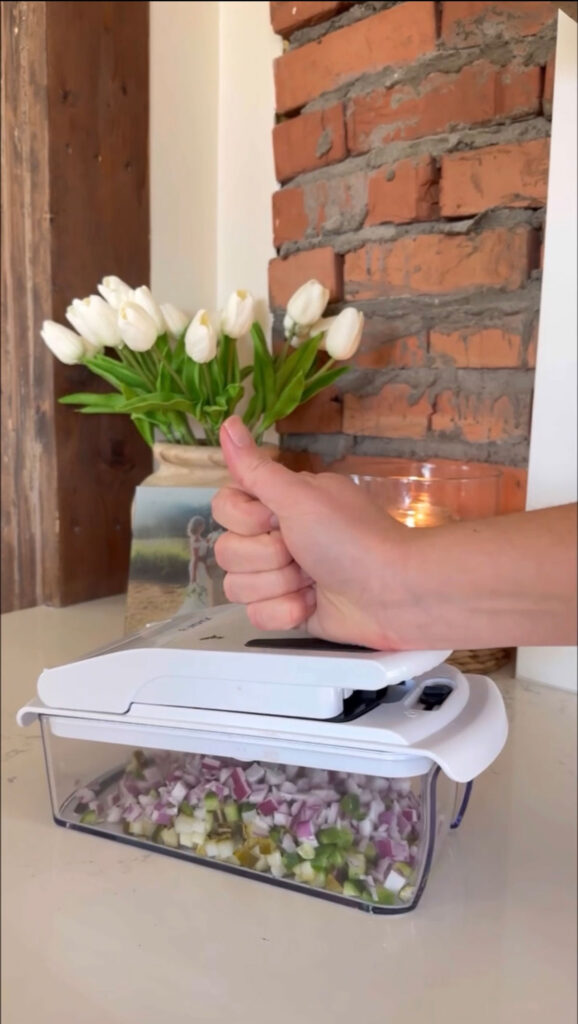 A hand using a chopper to make pickle salsa.