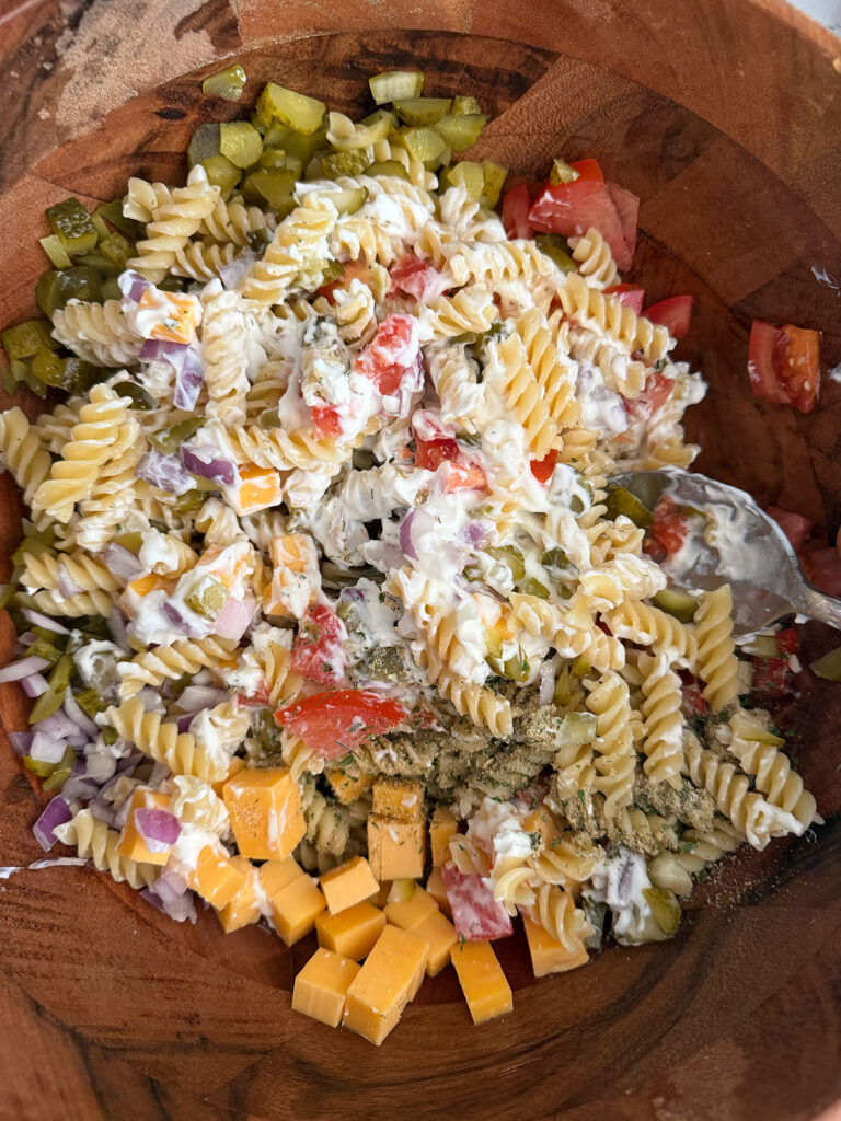 A wooden bowl with dressing added to dill pickle pasta salad.
