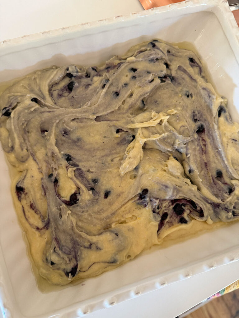 Blueberry cake batter is spread into the bottom of a white baking dish.