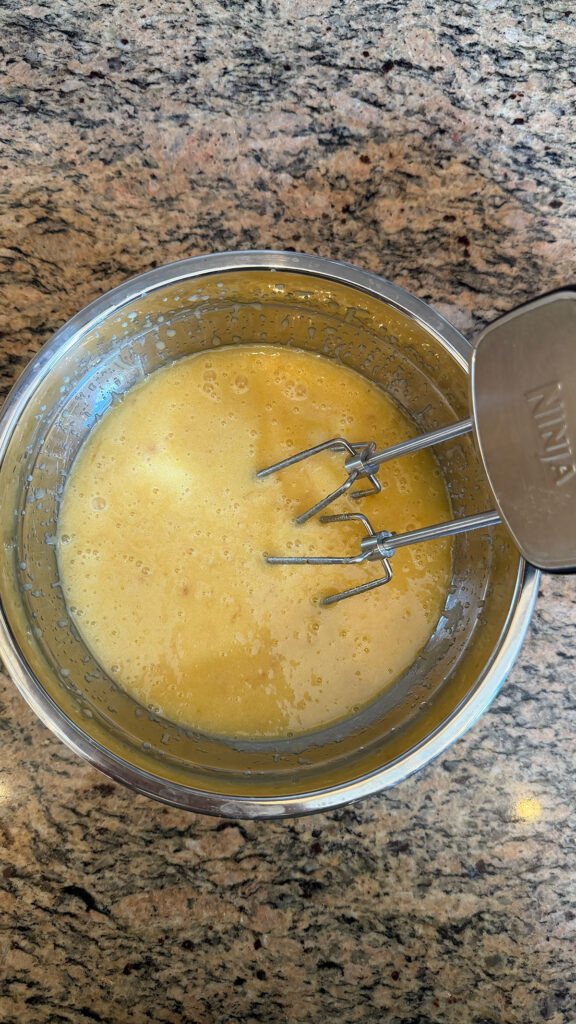 A metal bowl with a hand mixer with wet ingredients for strawberry bundt cake.