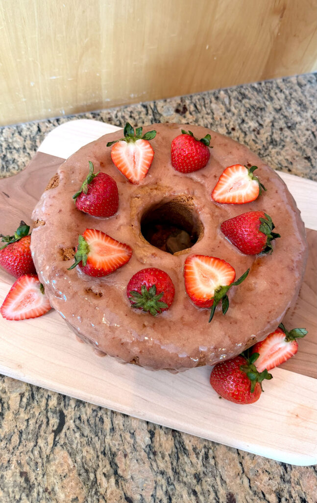 A glazed strawberry bundt cake on a cutting board.