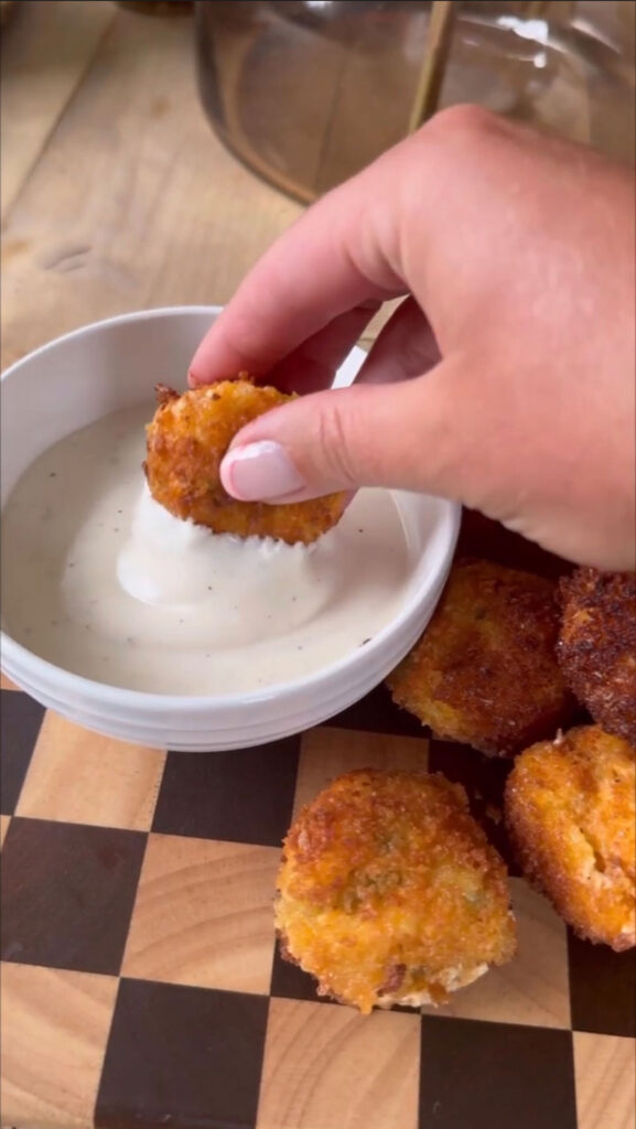 hand dipping fried pickle cheese ball into dip in white bowl