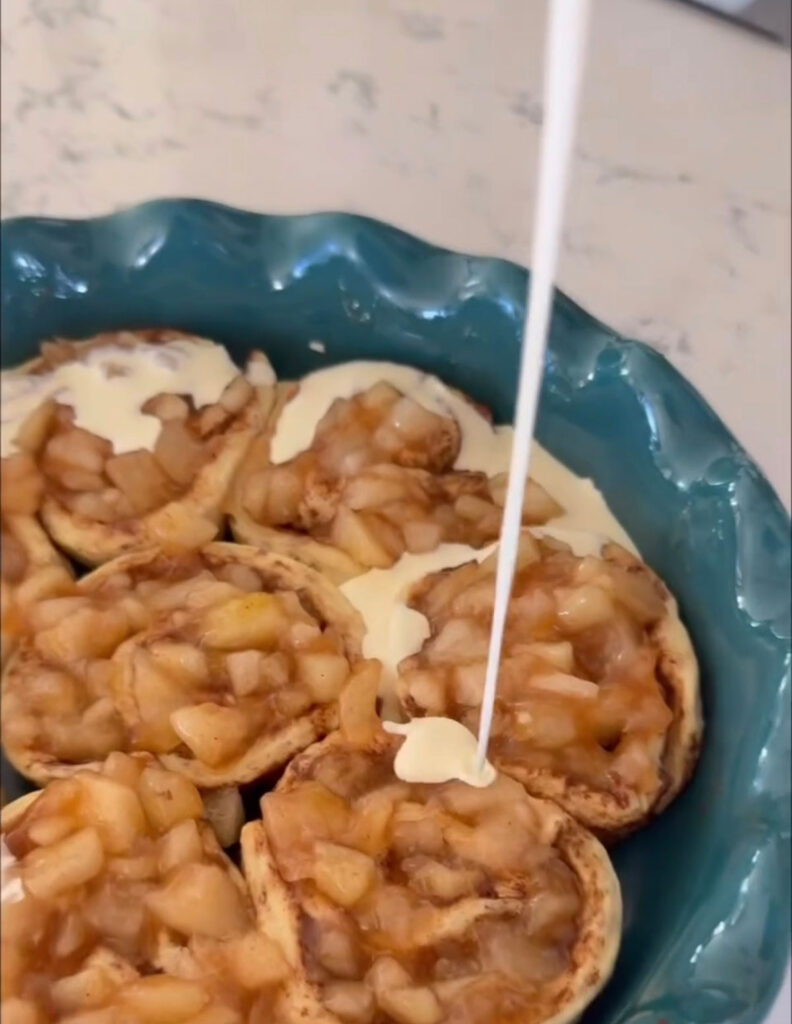 half and half being poured over top of apple pie cinnamon rolls in pie plate