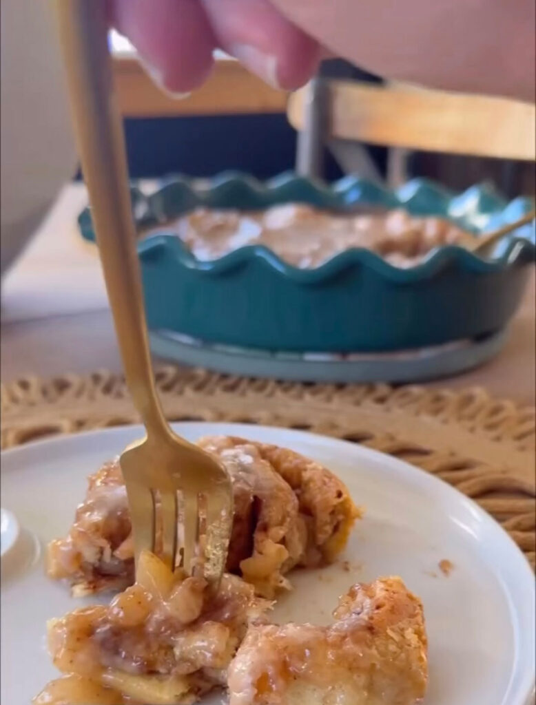 Apple pie cinnamon rolls on white plate with fork, with plate of cinnamon rolls in background