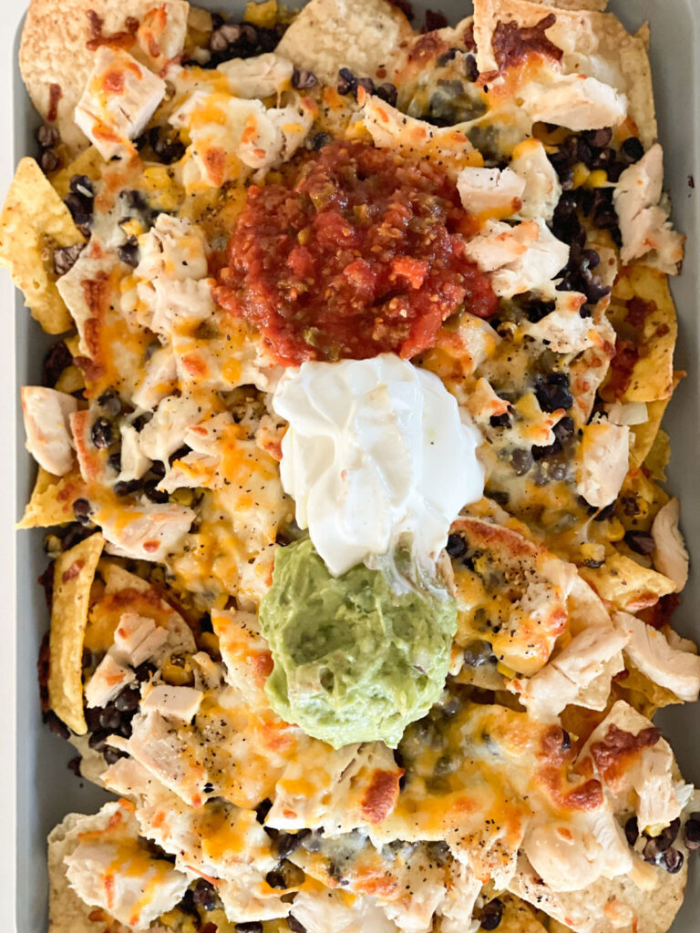 baked sheet pan nachos topped with salsa, sour cream and guacamole