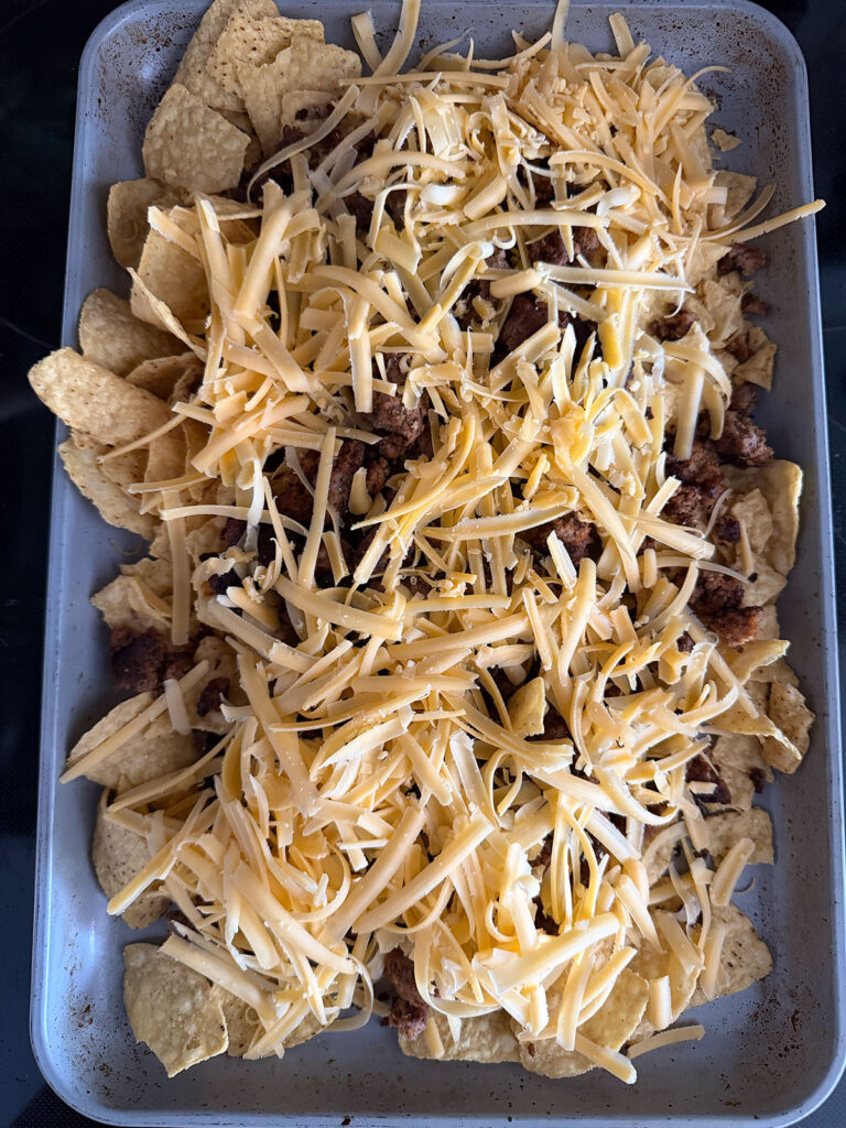 nachos being built on pan with chips, meat and shredded cheese