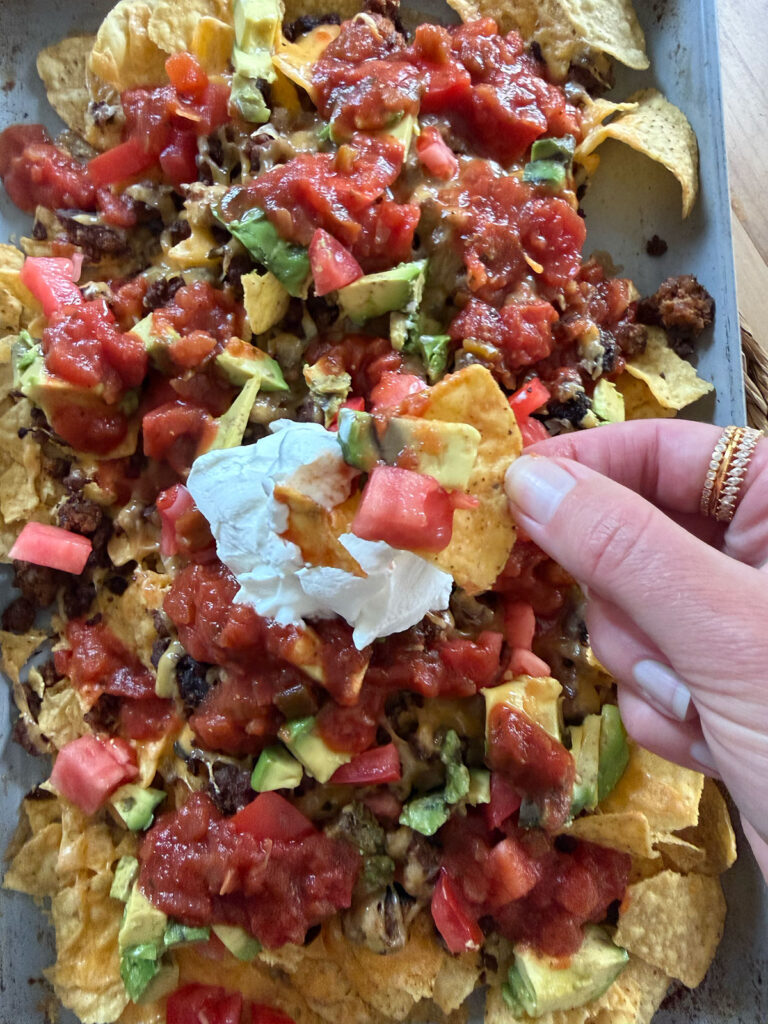 hand holding chip with toppings over sheet pan nachos