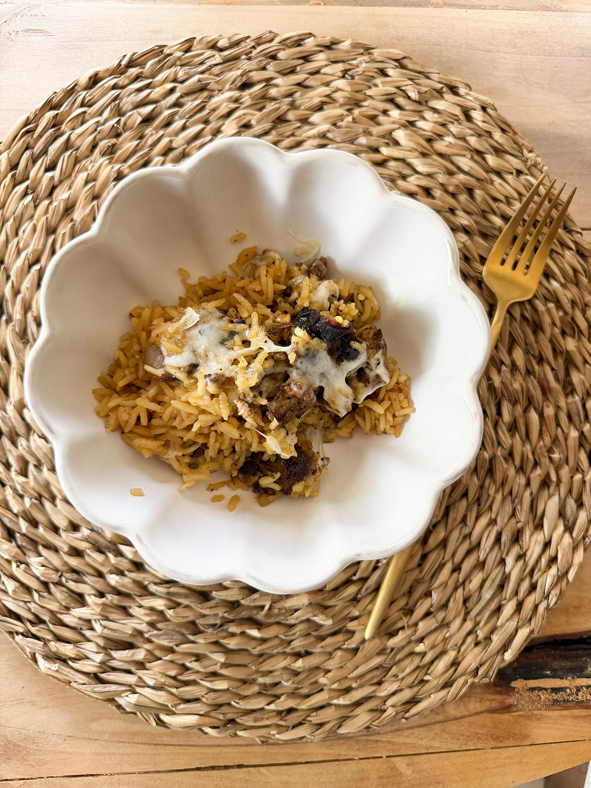 french onion ground beef casserole in white dish on placemat with gold fork next to it