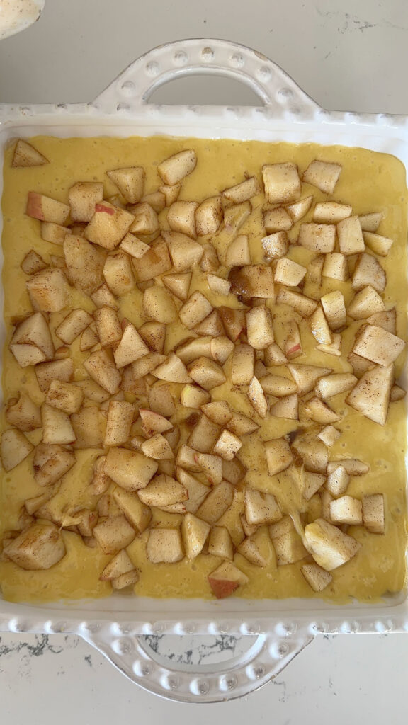 unbaked apple pie cake batter in baking dish topped with diced apples