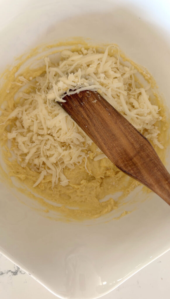 shredded cheese added to pizza muffin batter in white bowl
