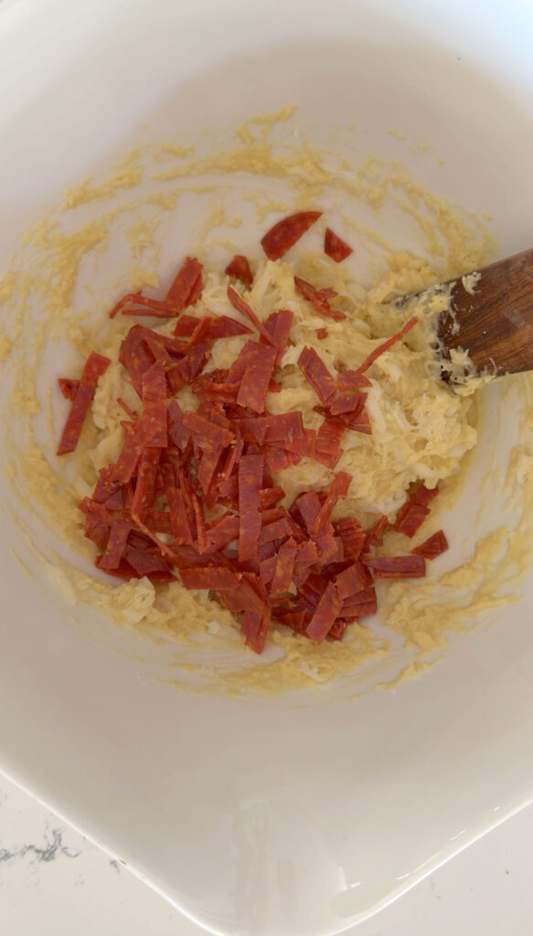strips of pepperoni added to pizza muffin batter in white bowl