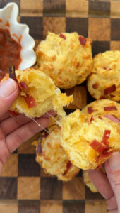 Hand pulling apart a baked pizza muffin with more baked pizza muffins below, next to a side of marinara sauce