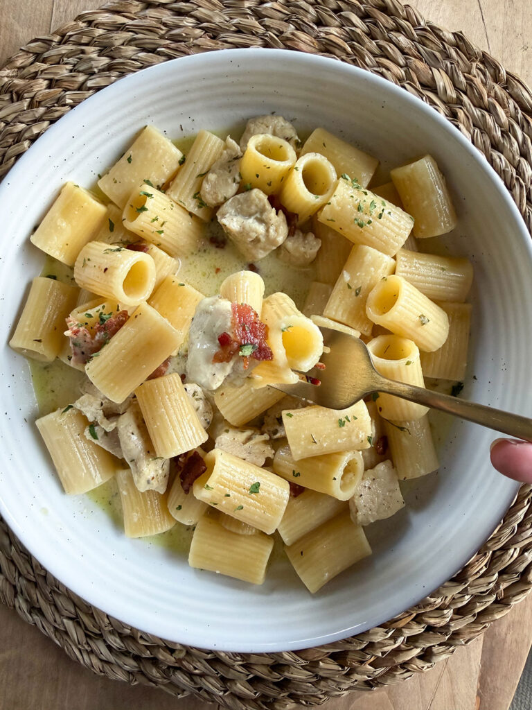 finished plate of chicken bacon ranch pasta with a gold fork taking a forkful. plate on placemat