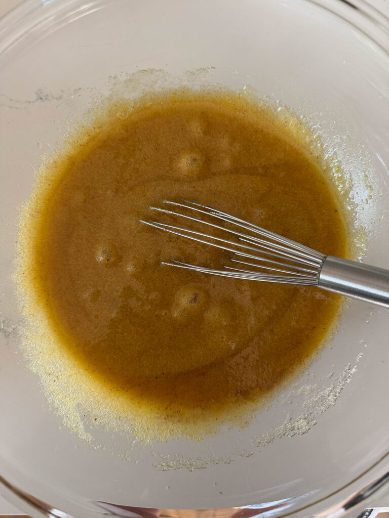 liquid batter ingredients in glass bowl with whisk