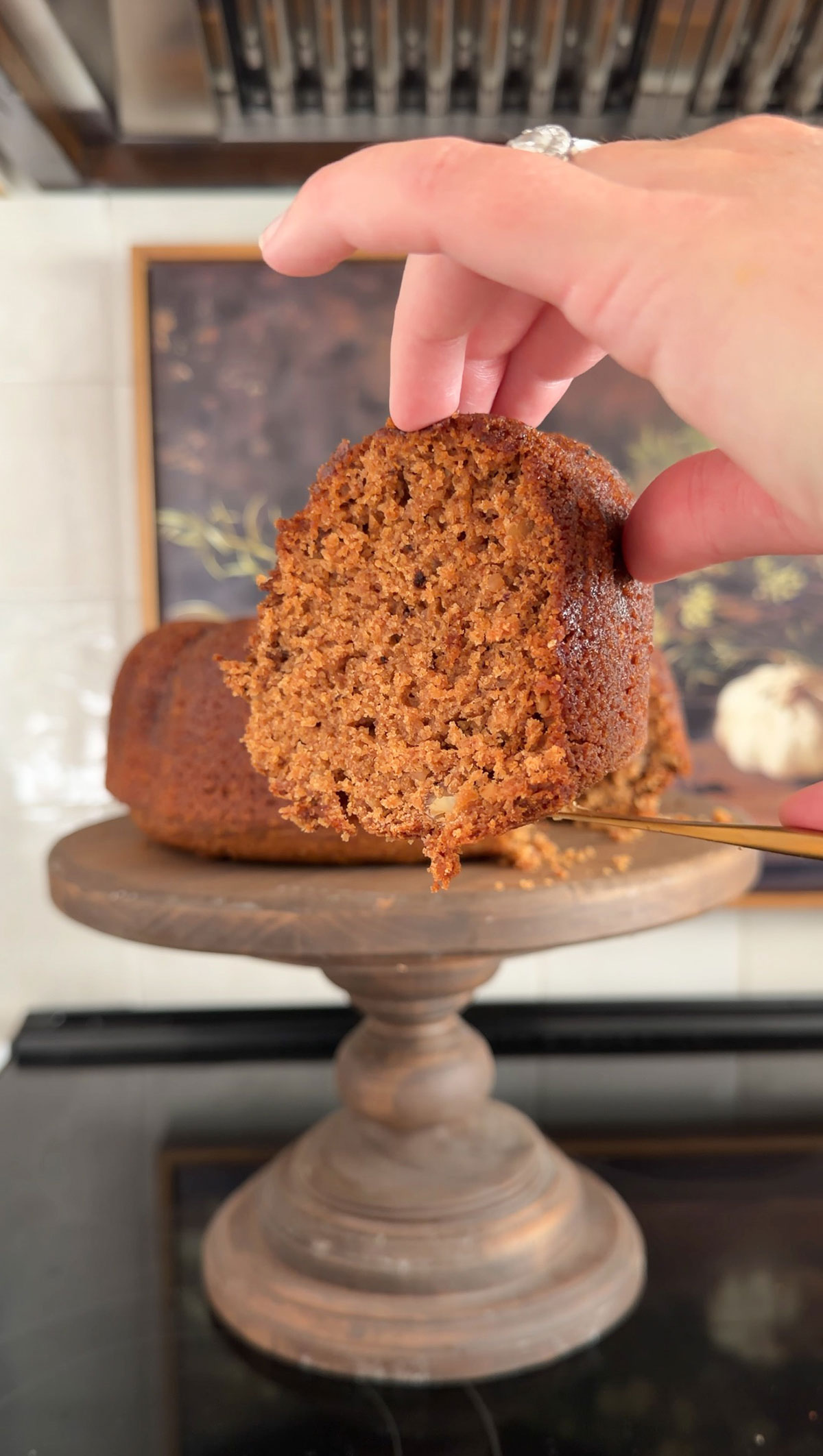 slice of applesauce cake being held up by hand with rest of cake on cake stand in background