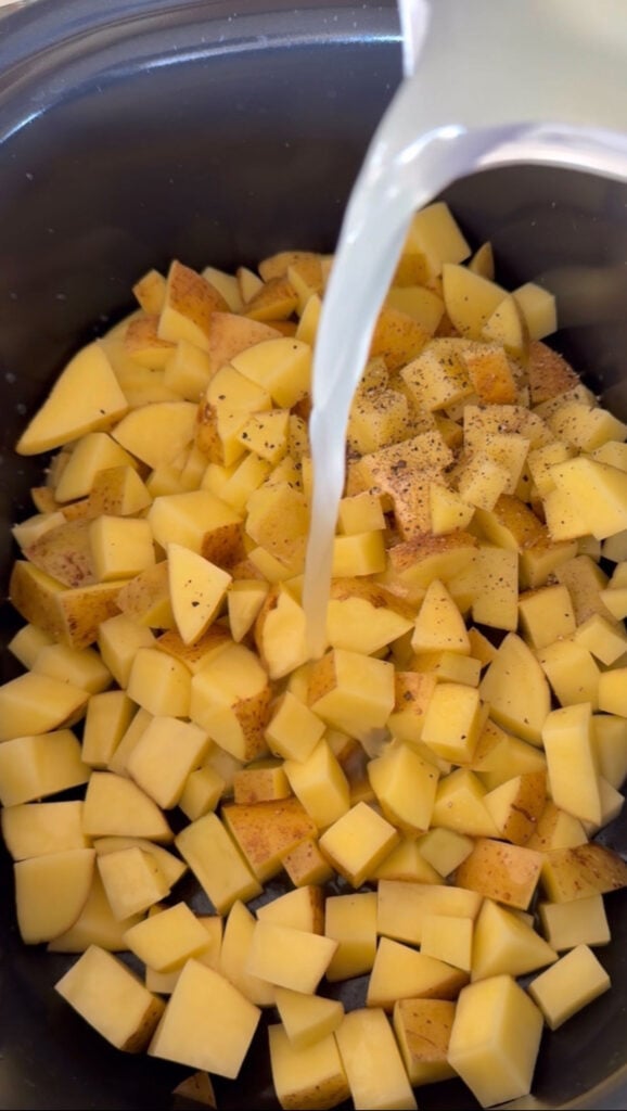 liquid being poured into crock pot with diced potatoes