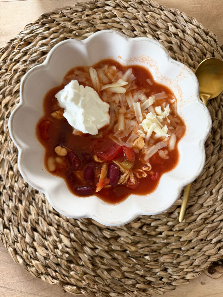 turkey chili in white bowl with dollop of sour cream and gold spoon on side