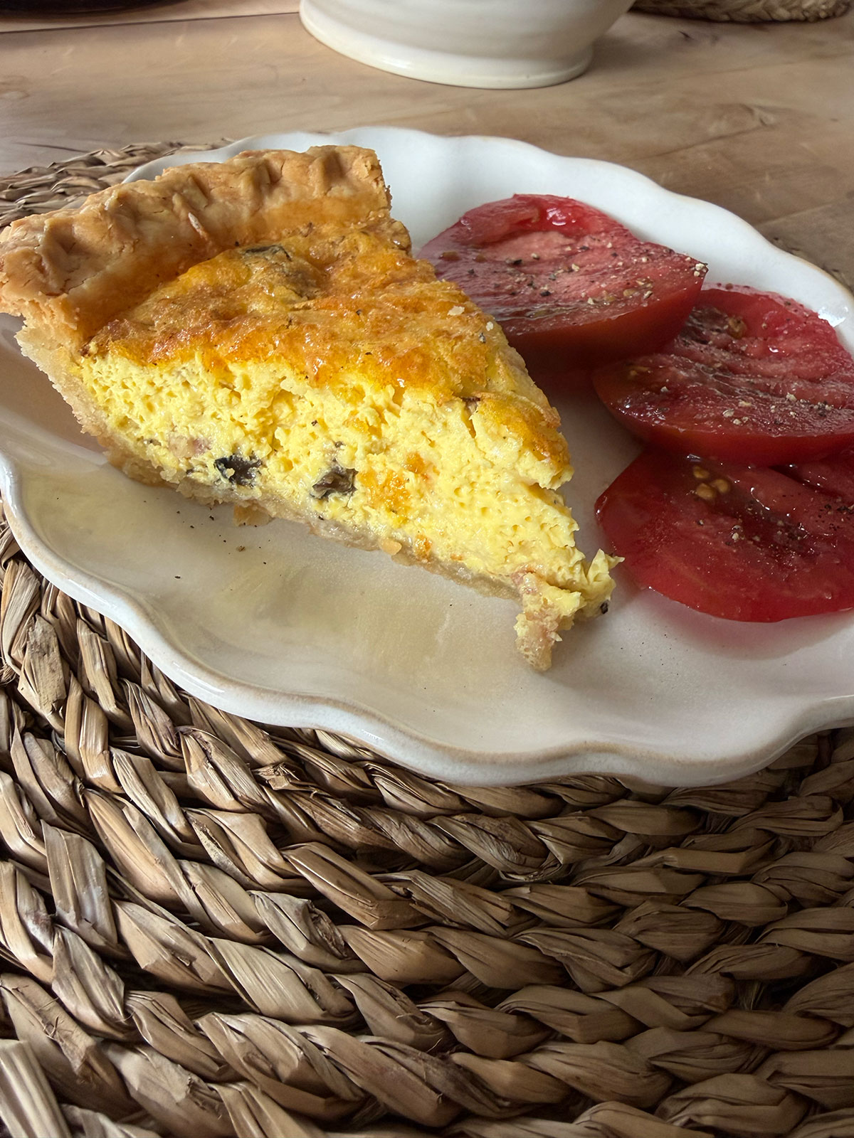 slice of quiche on white plate next to tomato slices
