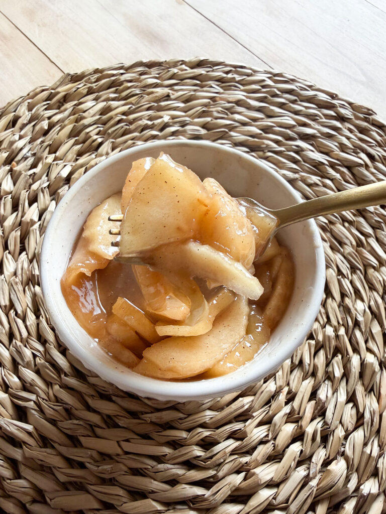 slow cooker cinnamon apples in white bowl with gold fork