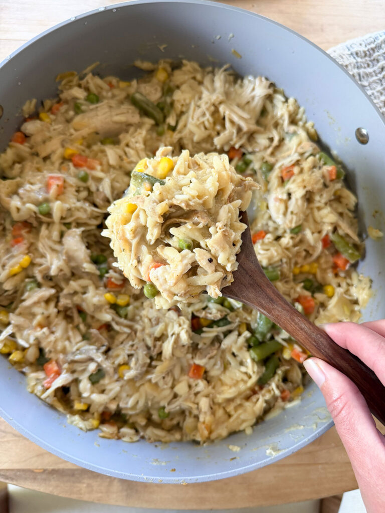 wooden spoonful of chicken pot pie orzo in pot below
