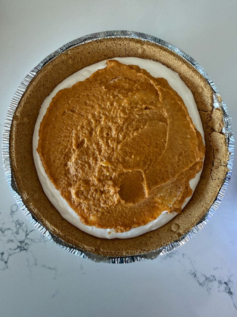 crust with whipped topping and pumpkin filling in it