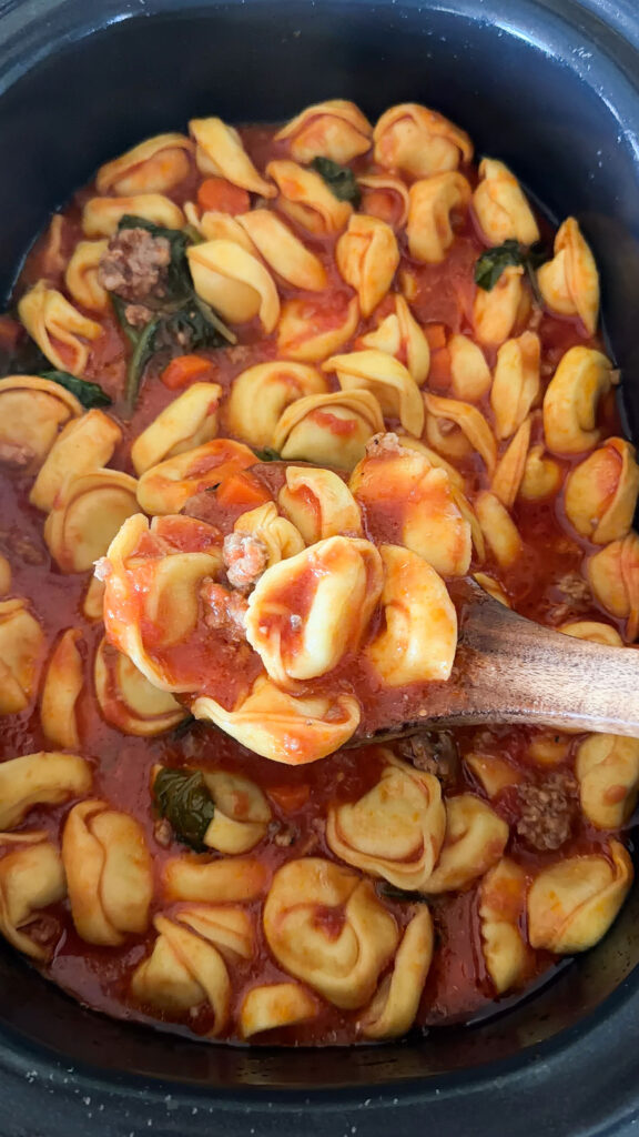 slow cooker of sausage tortellini soup with wooden spoon in it