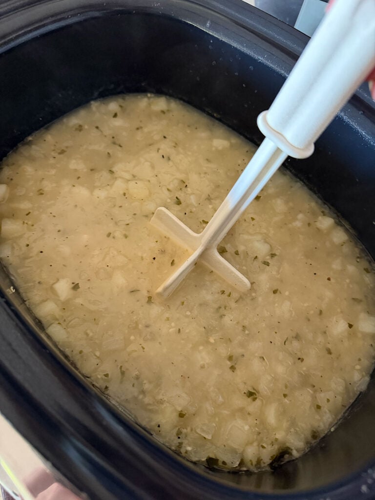 masher mashing potatoes in crockpot