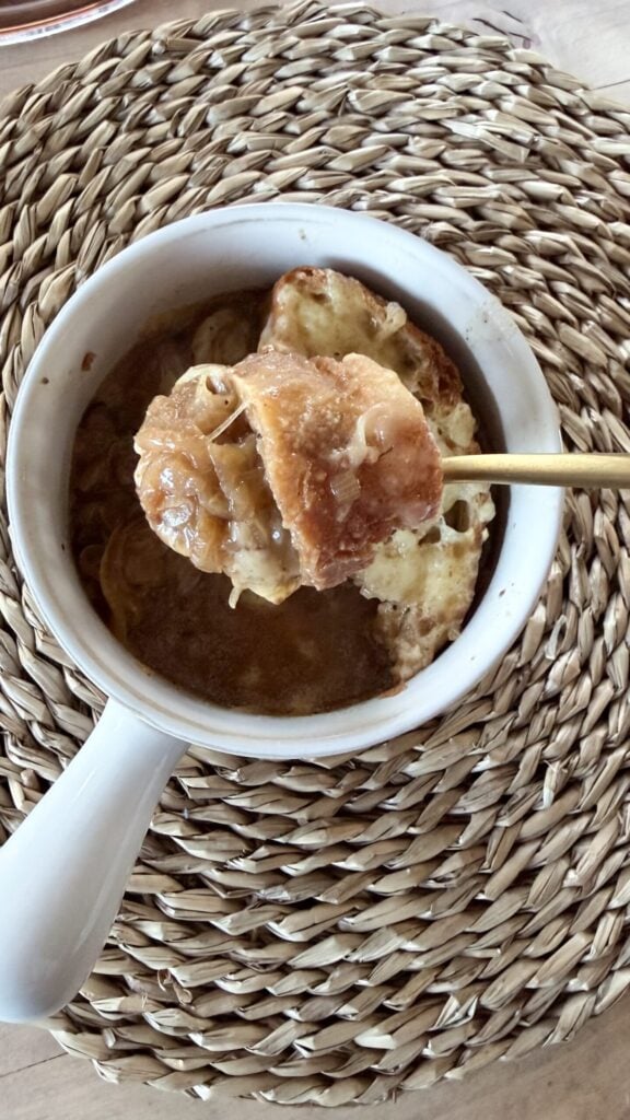 overhead shot of white crock full of french onion soup and gold spoonful raised