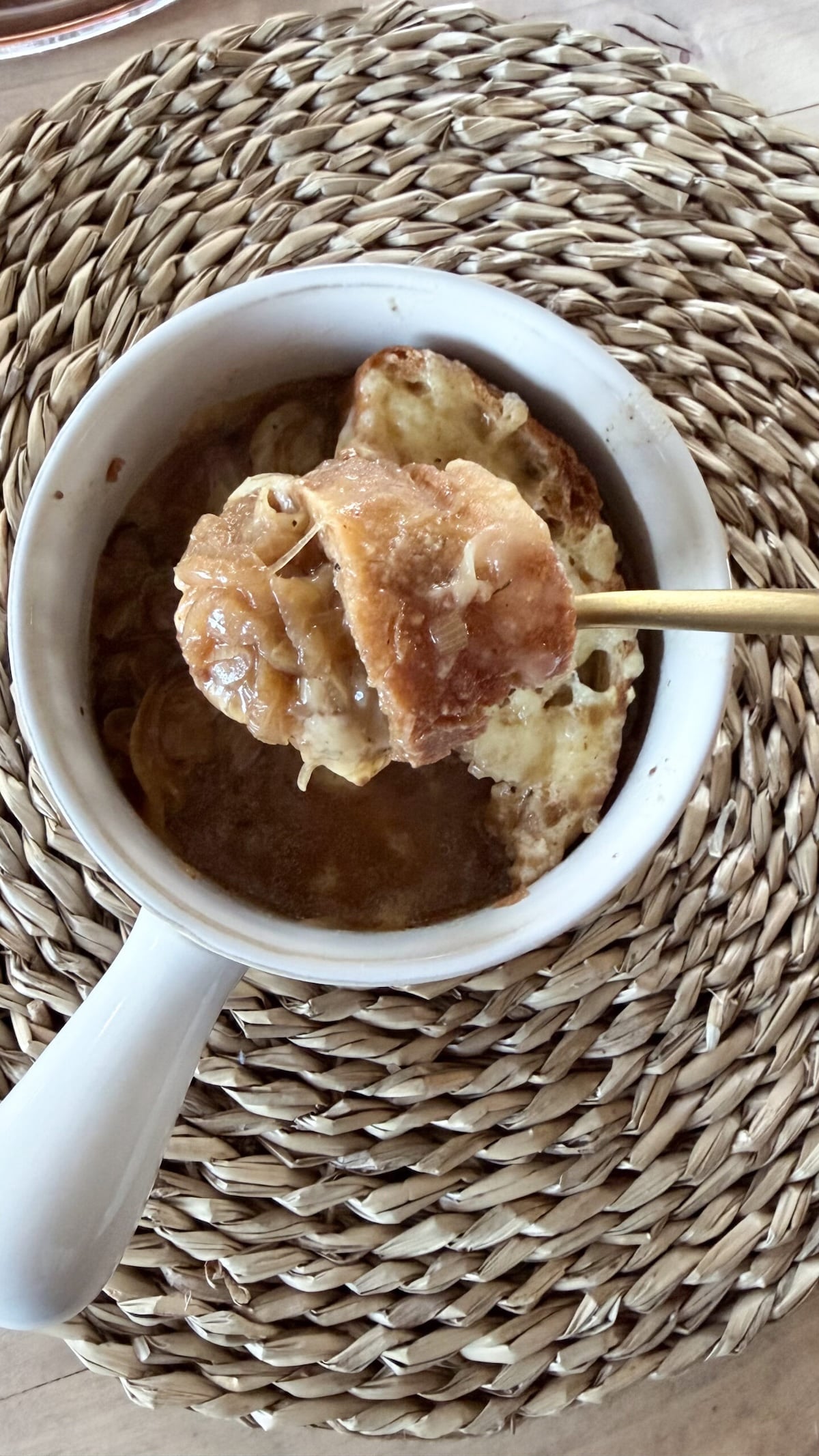 overhead shot of white crock full of french onion soup and gold spoonful raised