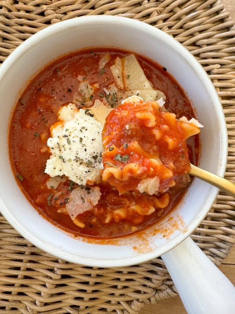 Overhead image of a white bowl with a gold spoon scooping out a spoonful of lasagna soup. 