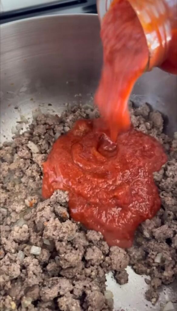 Ground beef cooking with jarred sauce being added in.