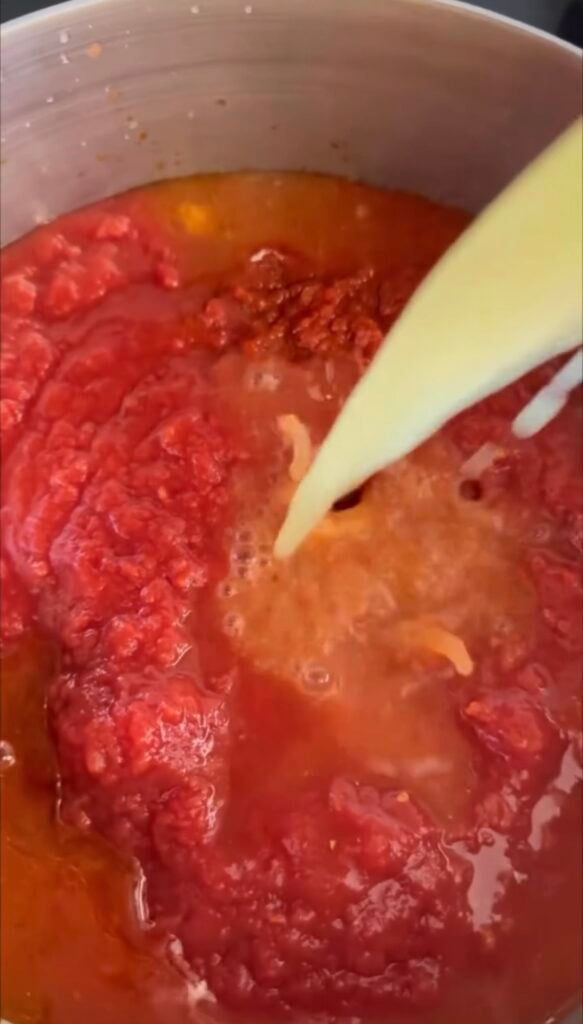 Adding broth to the beef and sauce in a pot. 