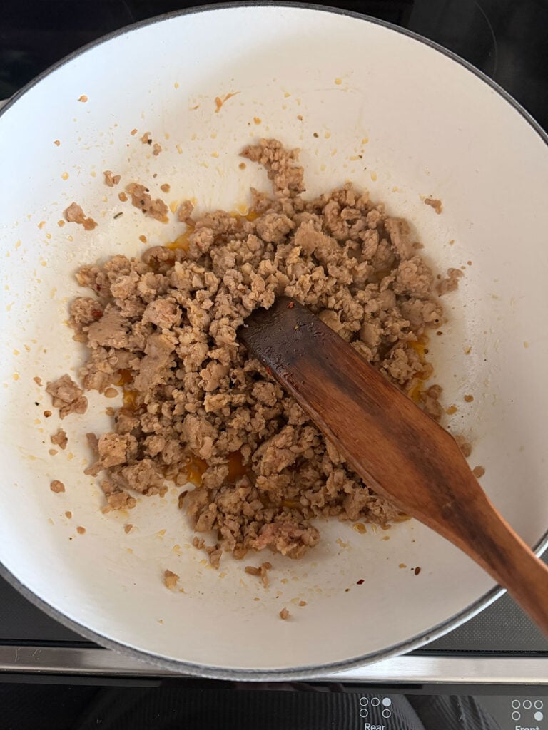 A saute pan cooking ground beef with wooden spoon.