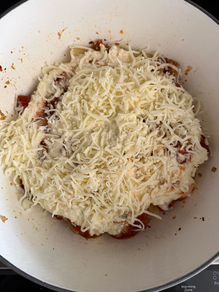 A pot with rigatoni noodles with cheese and sauce on top.