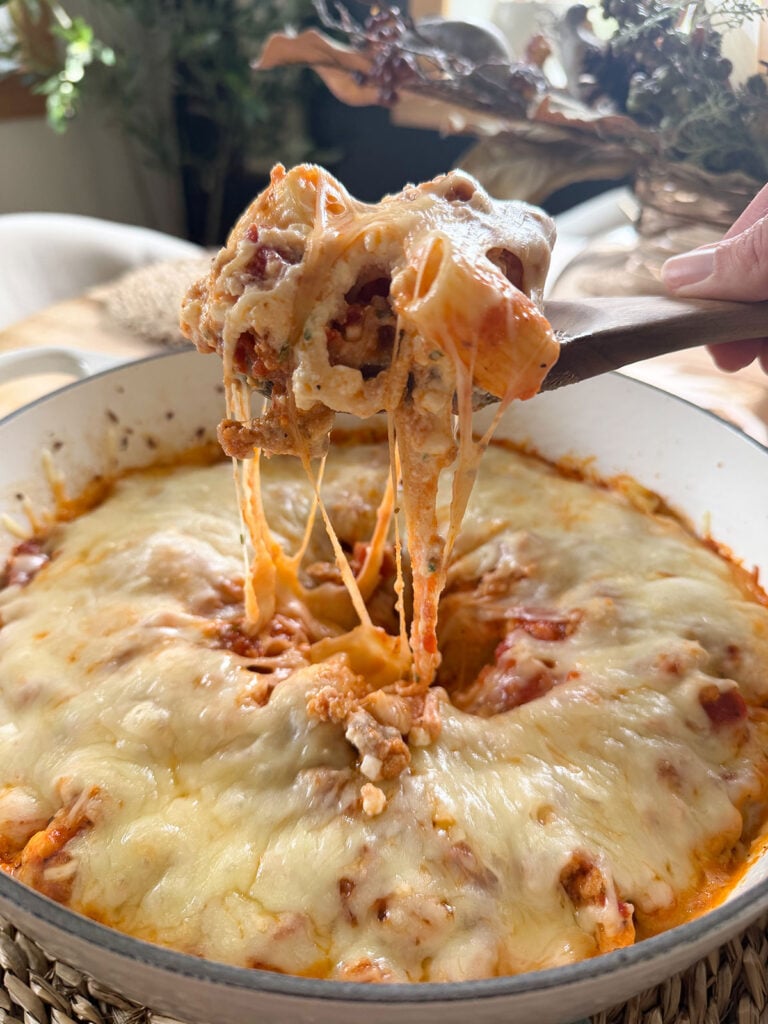 A hand taking a scoop out of baked rigatoni on a wooden spoon.