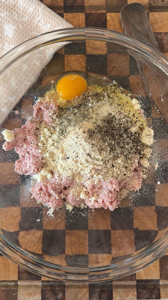 A glass bowl with ingredients for chicken parm meatballs.