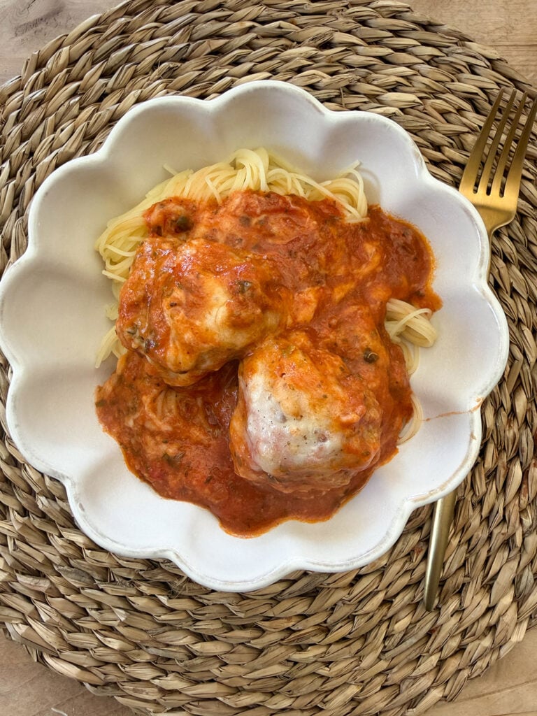 A white bowl with noodles and chicken parm meatballs on top.