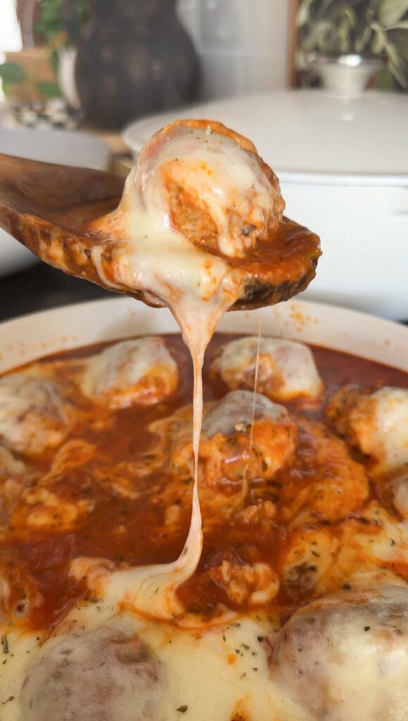 A wooden spoon lifting a chicken parm meatball out of the skillet.