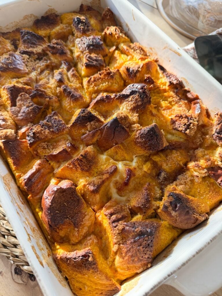 Side image of baked pumpkin french toast casserole in a white baking dish.