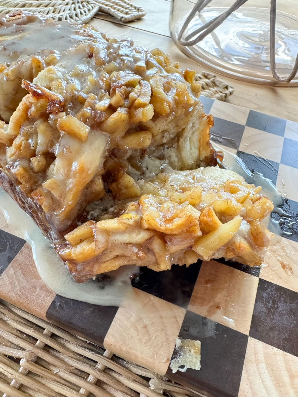 apple pie bread topped with glaze on checkered board with a slice cut into it